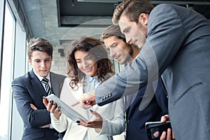 Group of businesspeople using a digital tablet together in front of office windows.