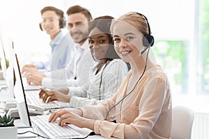 Group of call centre employees smiling and working on computers at light office, copy space