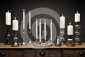 A group of candle sticks and glowing candles, shot on a wooden table, with a dark grey background