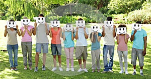 Group of casual young friends holding smiley faces over their faces