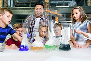 Group of caucasian school children in chemical lab. Pupils put dry ice into the flasks with colorful liquids which