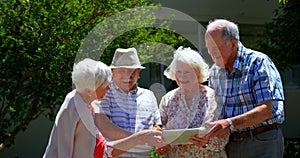 Group of Caucasian senior couples discussing over digital tablet in the garden of nursing home 4k