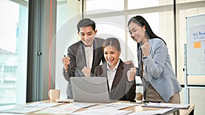 A group of cheerful Asian businesspeople are looking at a laptop screen, celebrating their good news