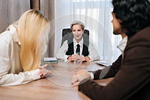 Group of cheerful business people having conversation sitting at desk in conference room, gathered for project