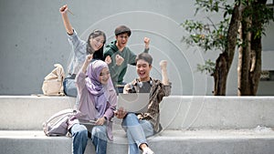 A group of cheerful diverse college students is looking at a laptop screen and showing their fist