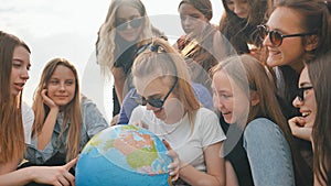 A group of cheerful girls is exploring the globe of the world in the meadow.