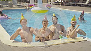 Group of cheerful multiethnic male friends dancing in pool at resort. Portrait of happy young Middle Eastern and