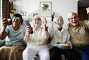 Group of cheerful senior friends sitting and watching TV together photo