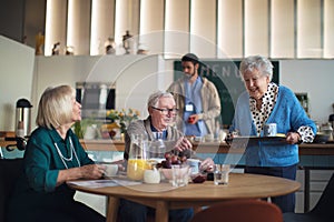 Group of cheerful seniors enjoying breakfast in nursing home care center.