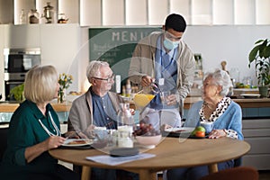 Group of cheerful seniors enjoying breakfast in nursing home care center.