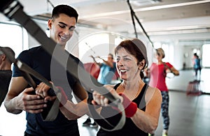 A group of cheerful seniors in gym with a young trainer doing exercise with TRX.