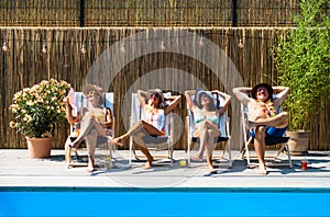 Group of cheerful seniors sitting by swimming pool outdoors in backyard.