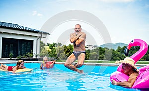 Group of cheerful seniors in swimming pool outdoors in backyard, jumping.