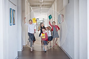 A group of cheerful small school kids in corridor, running and jumping.