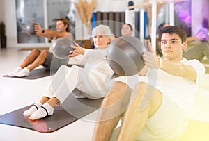 Group of cheerful sports people of different ages practicing pilates with a ball in the gym of a modern fitness studio.