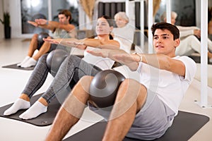 Group of cheerful sports people of different ages practicing pilates with a ball in the gym of a modern fitness studio.