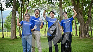 A group of cheerful young Asian volunteers is standing in a public park with garbage bags