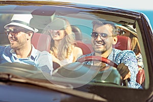 Group of cheerful young friends driving car and smiling in summer
