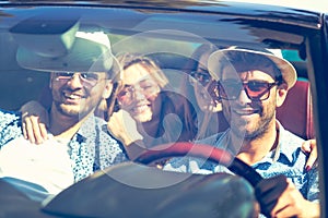 Group of cheerful young friends driving car and smiling in summer