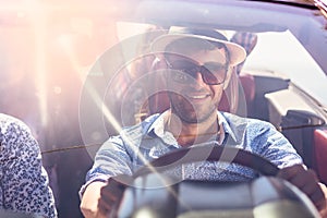 Group of cheerful young friends driving car and smiling in summer