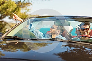 Group of cheerful young friends driving car and smiling in summer