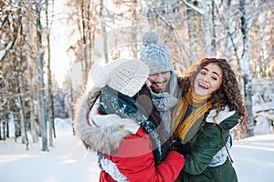 A group of cheerful young friends having fun outdoors in snow in winter forest.