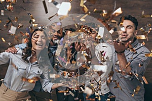 Group of cheerful young people standing together and celebrating with confetti