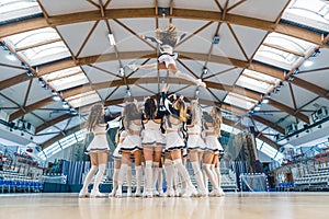 Group of cheerleaders performing stunt lifting fellow up in the air in an arena