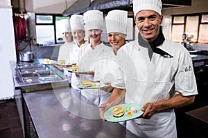 Group of chefs holding plate of delecious desserts in kitchen