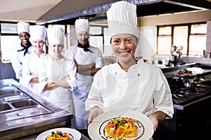 Group of chefs holding plate of prepared pasta in kitchen