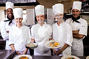 Group of chefs holding plate of prepared pasta in kitchen