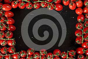 Group of cherry tomatoes on black marble like board, arranged in frame around, rectangular space for text in middle