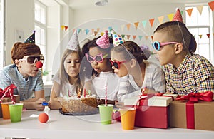 Group of children all together blowing candles on birthday cake at fun party at home