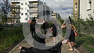 Group of children in black masquerade costumes are running down the street. Halloween. Back view.