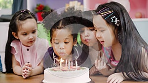 Group of children celebrate birthday`s party in classroom, Multi-ethnic young boys and girls happy make a wish blow out candles o