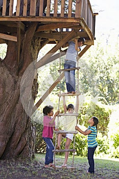 Group Of Children Climbing Rope Ladder To Treehouse