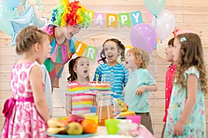 Group of children with clown blowing candles on cake at birthday party