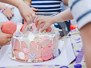 Group of children eating cake outdoors by fingers. Close-up.