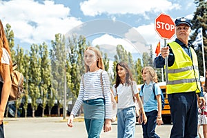 Group of children going out the school bus crossing road while driver holding stop sign attentive