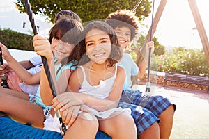 Group Of Children Having Fun On Swing In Playground