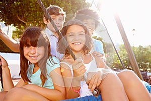 Group Of Children Having Fun On Swing In Playground