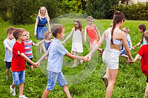 Group of children holding hands and dancing in circle on green lawn in park