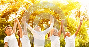 Group of children holding hands up in park on sunny day