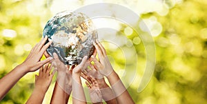 Group of children holding planet earth over defocused nature background