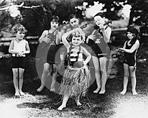 Group of children performing with instruments and one girl dancing the hula