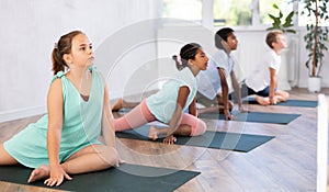 Group of children are practicing Hatha yoga for amateurs. Girl sits in pigeon pose,