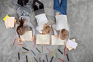 Group of children are reading books and drawing with pencils while lying on floor. Top view