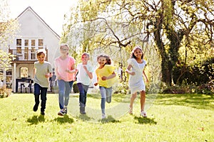 Group Of Children Running Across Garden Lawn At Home Looking Into Camera