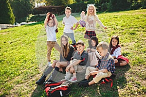 A group of children of school and preschool age are sitting on the green grass in the park.