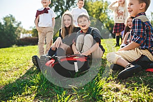 A group of children of school and preschool age are sitting on the green grass in the park.